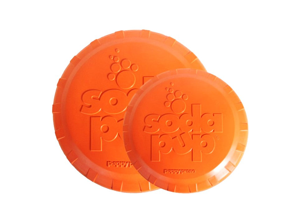 Orange Rubber Dog Frisbee by SodaPup, vet-approved, made in USA, durable toy for dogs, shown in outdoor setting.